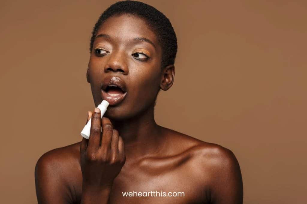 a beautiful black girl applying lip balm as an alternative for clinique black honey