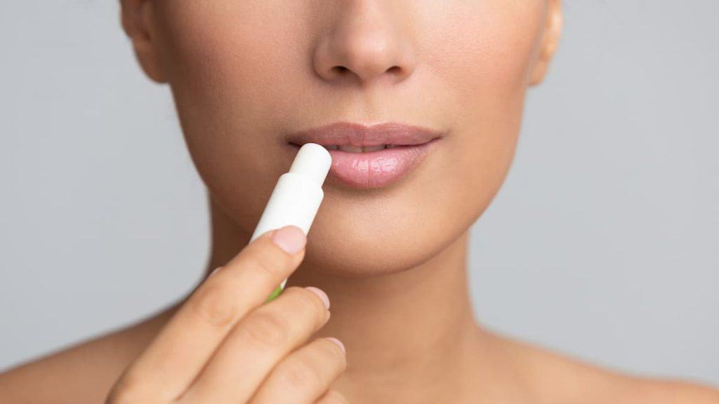 A woman is using a lip balm on her lips.