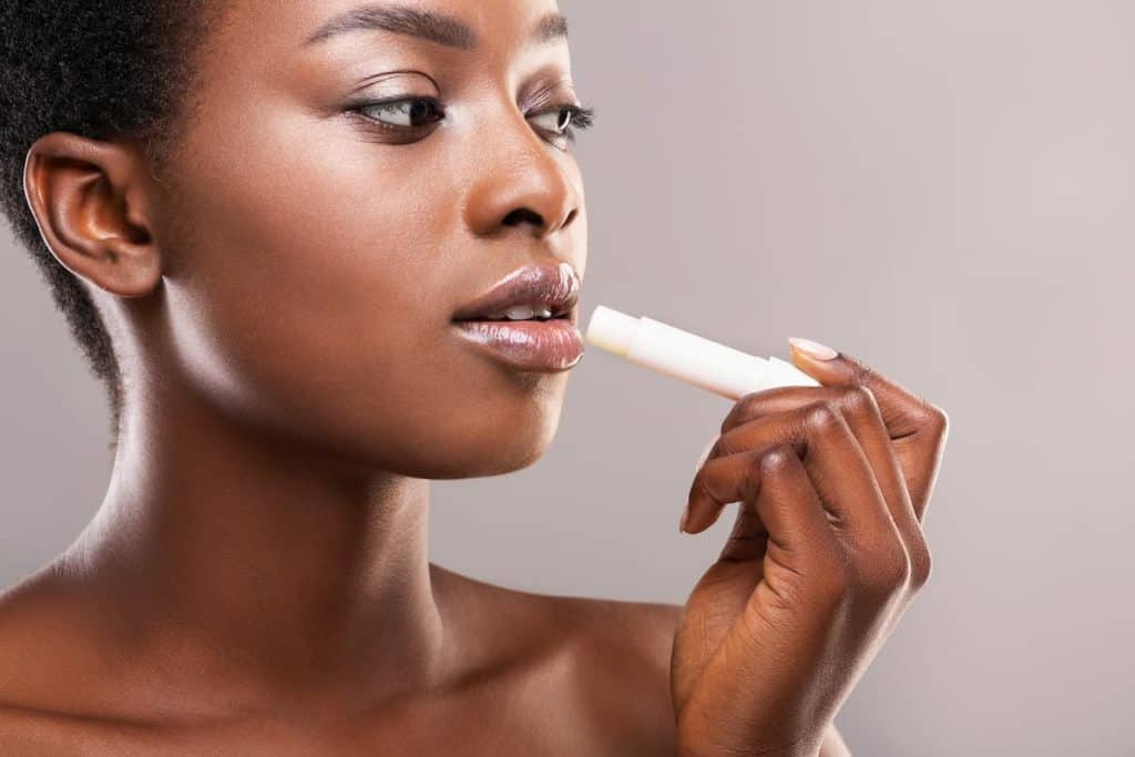 A black woman is using a lip balm on her lips.