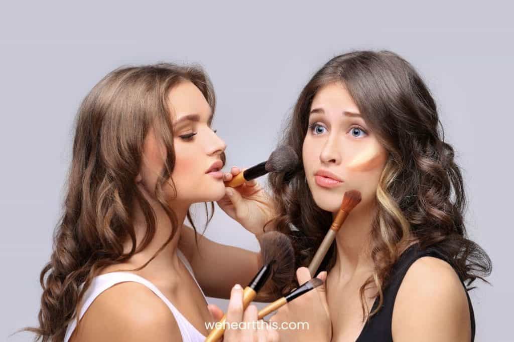 two young women applying cream bronzer to each other with a brush