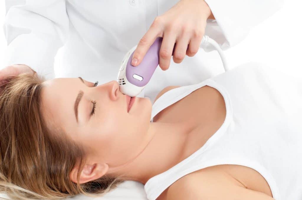 beautician using a face epilator on female client's face