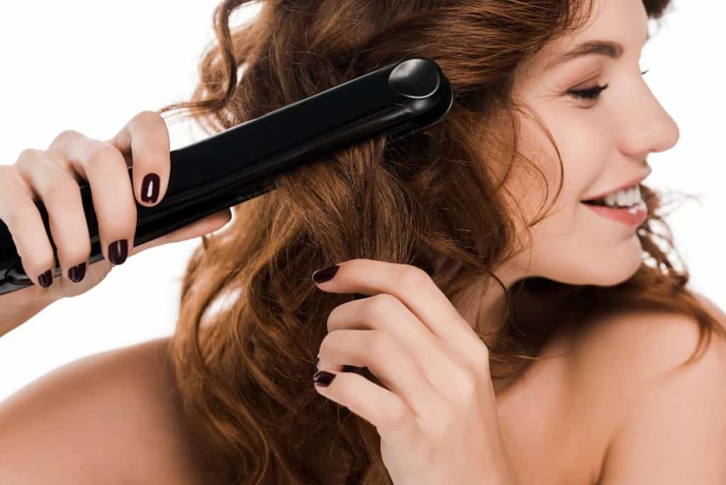 happy curly woman using flat iron or hair straightener isolated on white background