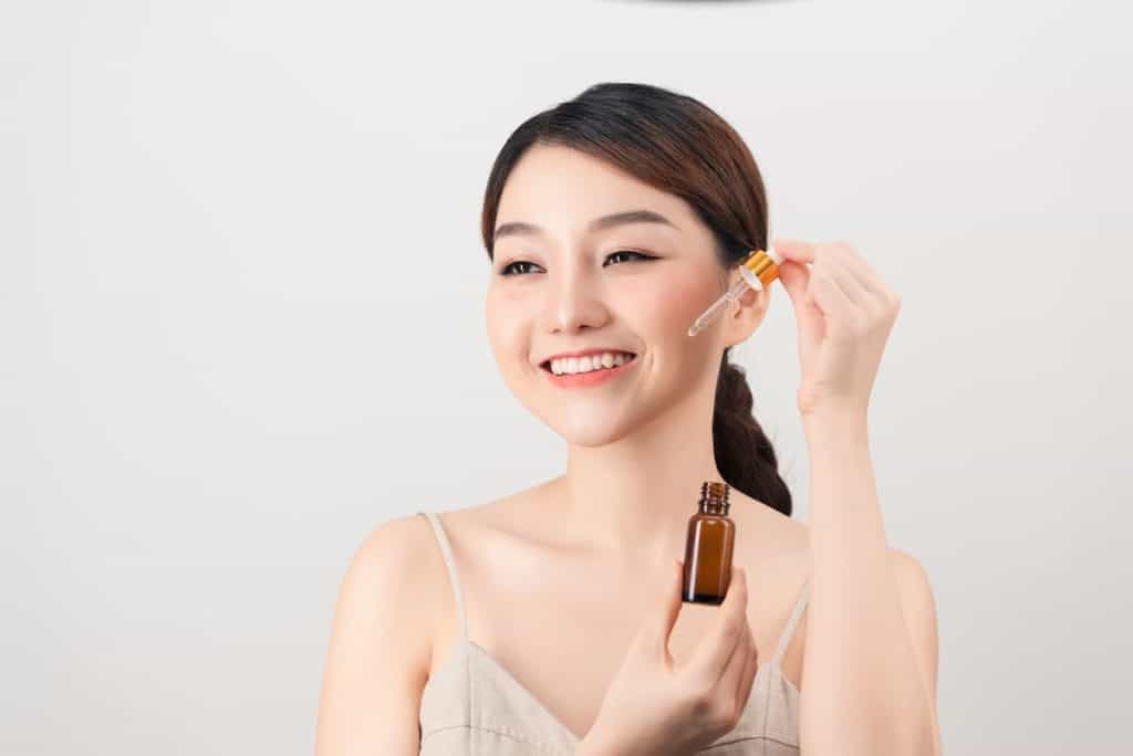 young amazing woman posing isolated over white background holding face serum