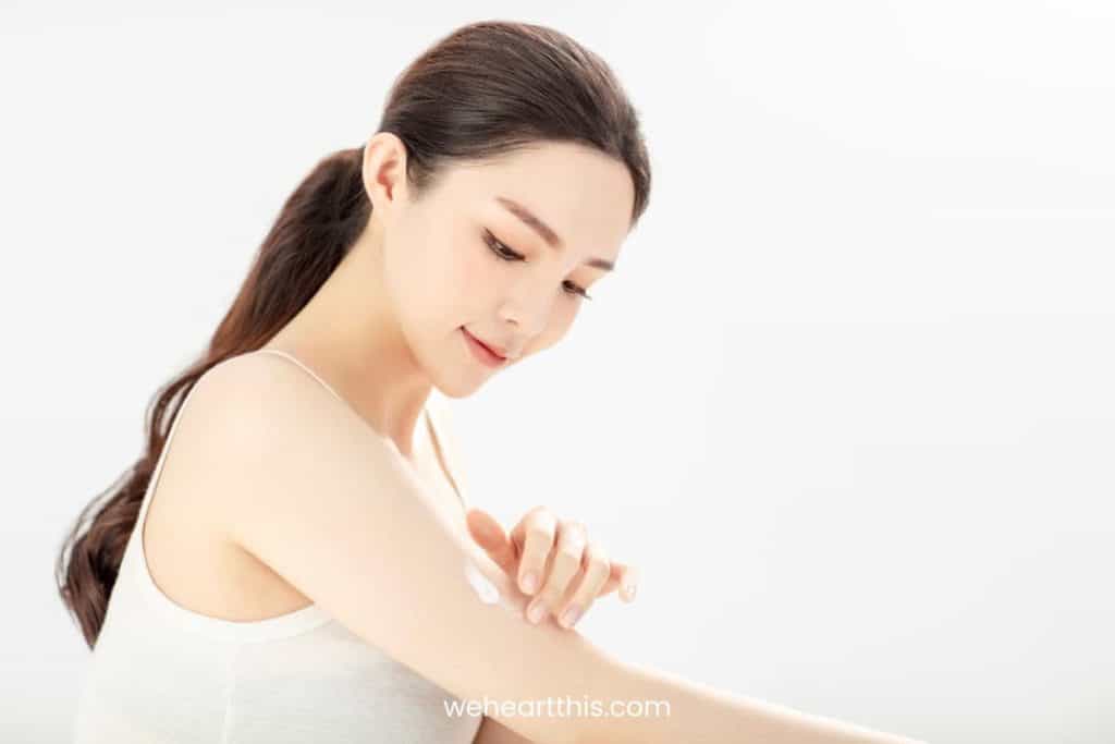 a young asian girl applying sunscreen as a moisturizer on her body and face