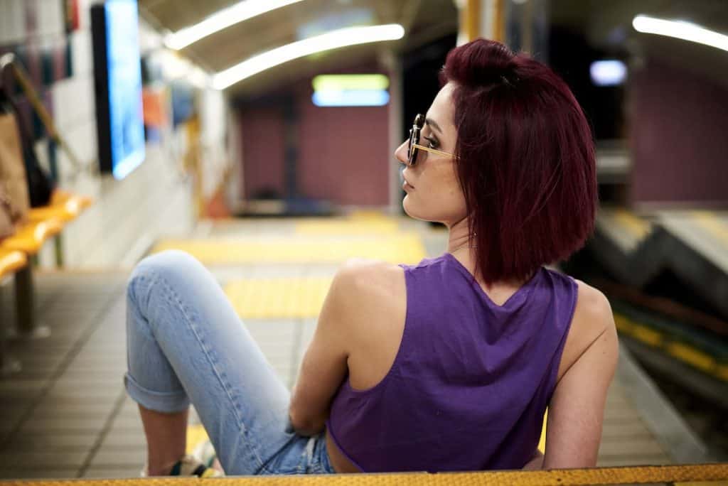 A girl with chocolate cherry short hair is sitting at a waiting station