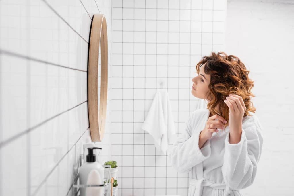 short curly haired woman applying hair product on her hair in a white bathroom