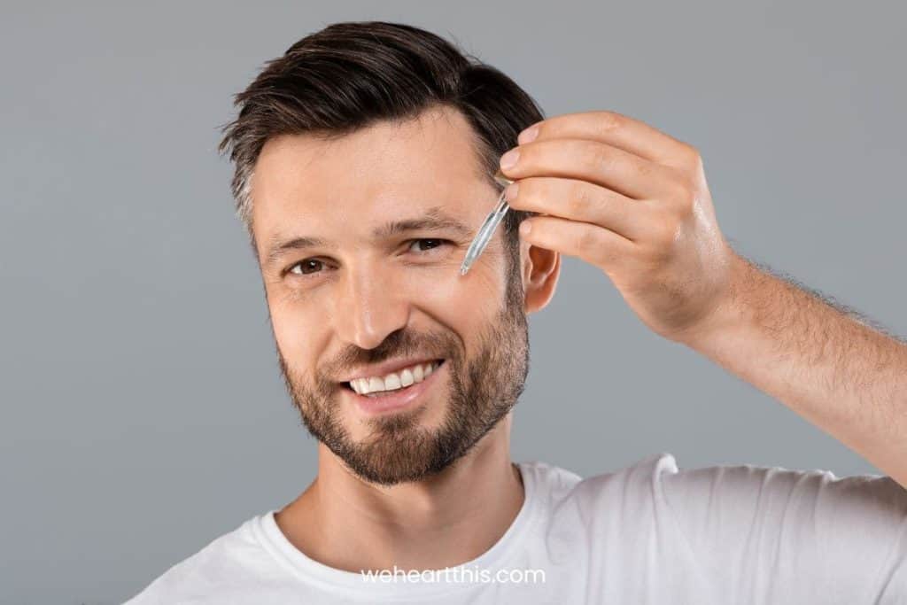 a middle-aged man applying granactive retinoid serum at face while smiling
