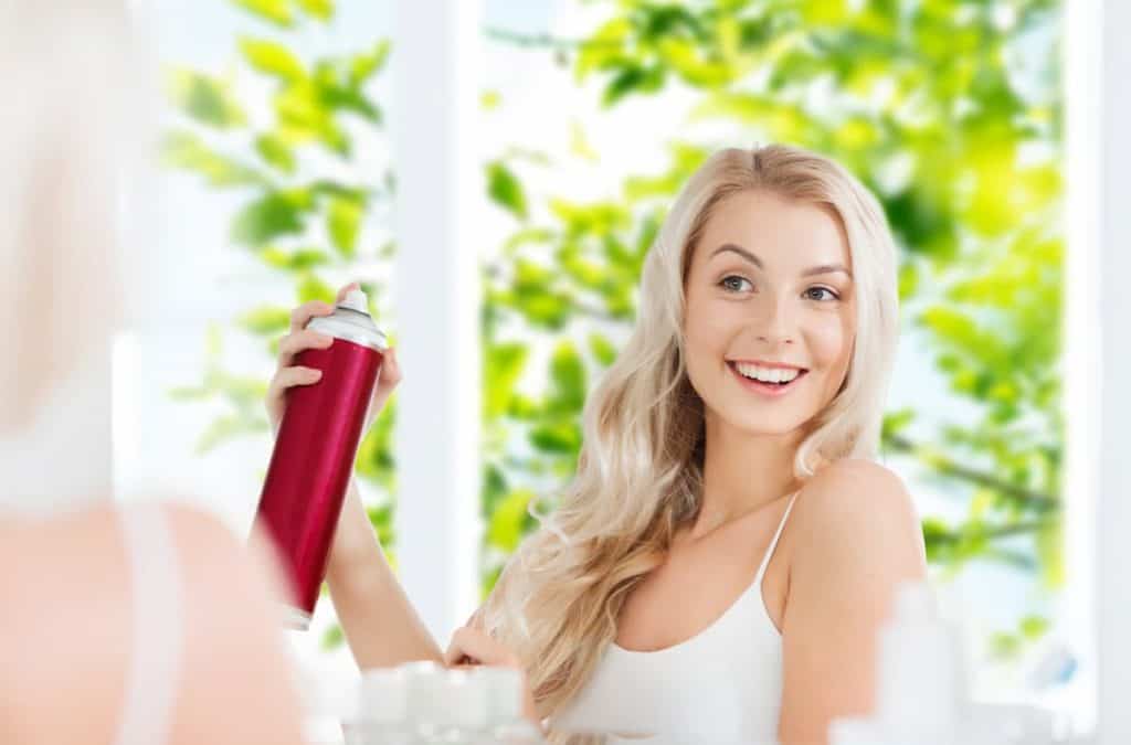 woman with hairspray styling her hair at bathroom