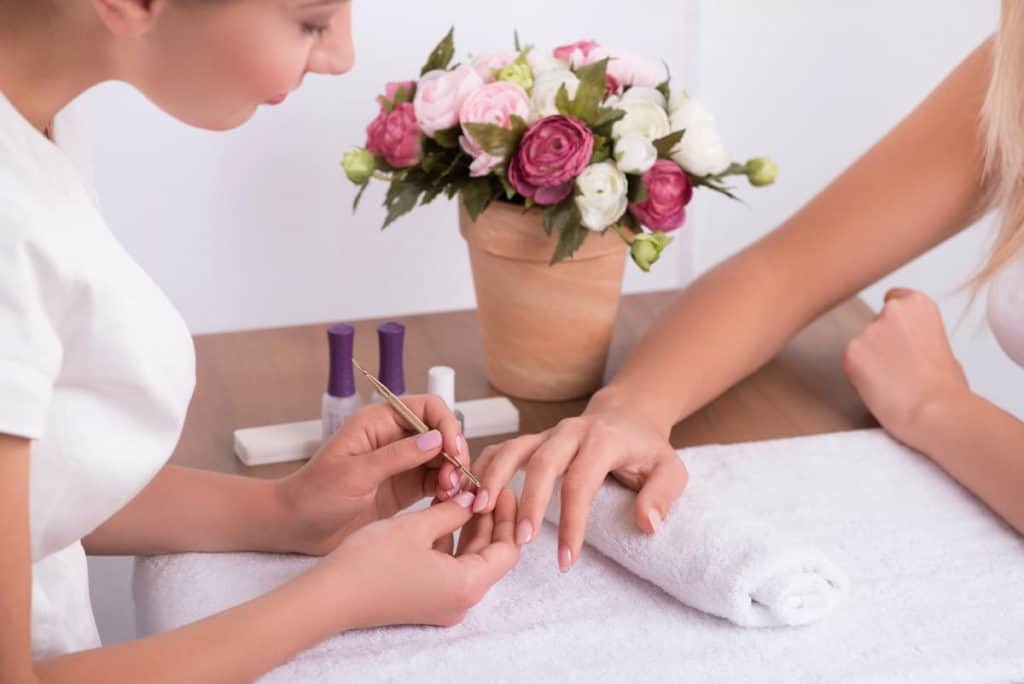 a manicurist cleaning the nails of the client under white towel