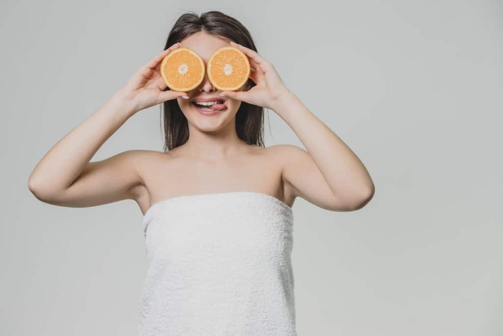 a young girl wrapped in white towel is raising her hands to pose with the orange fruit