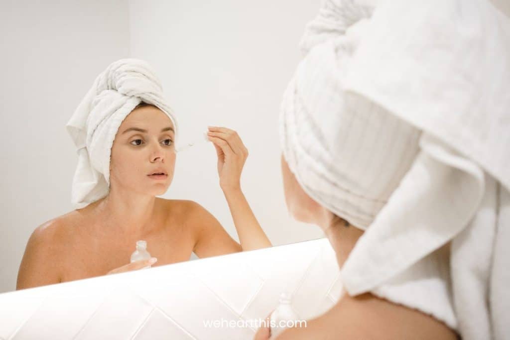 a girl with hair wrapped in towel is applying jojoba and roseship oil on face
