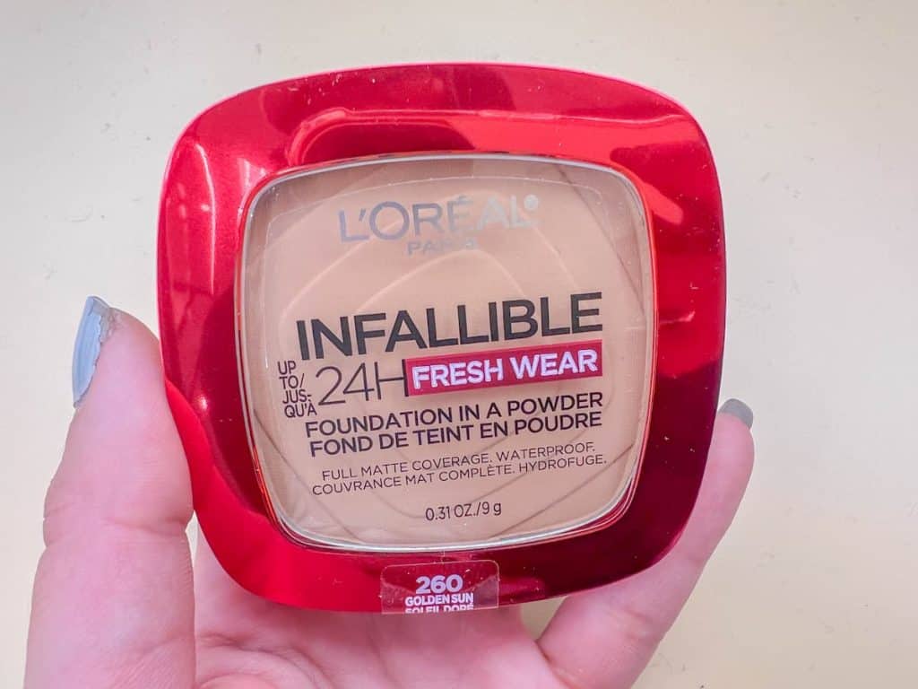 A woman's hand holding Loreal infallible 24 fresh wear foundation on a beige background