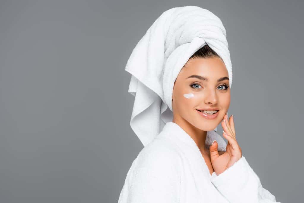 smiling woman with towel on head and cosmetic cream on face