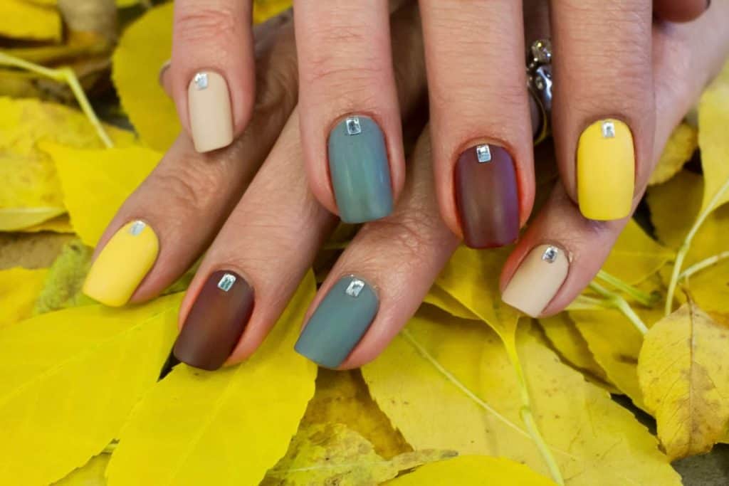 a close up image of a woman's hands painted with almond fall nails color palette under the leaves