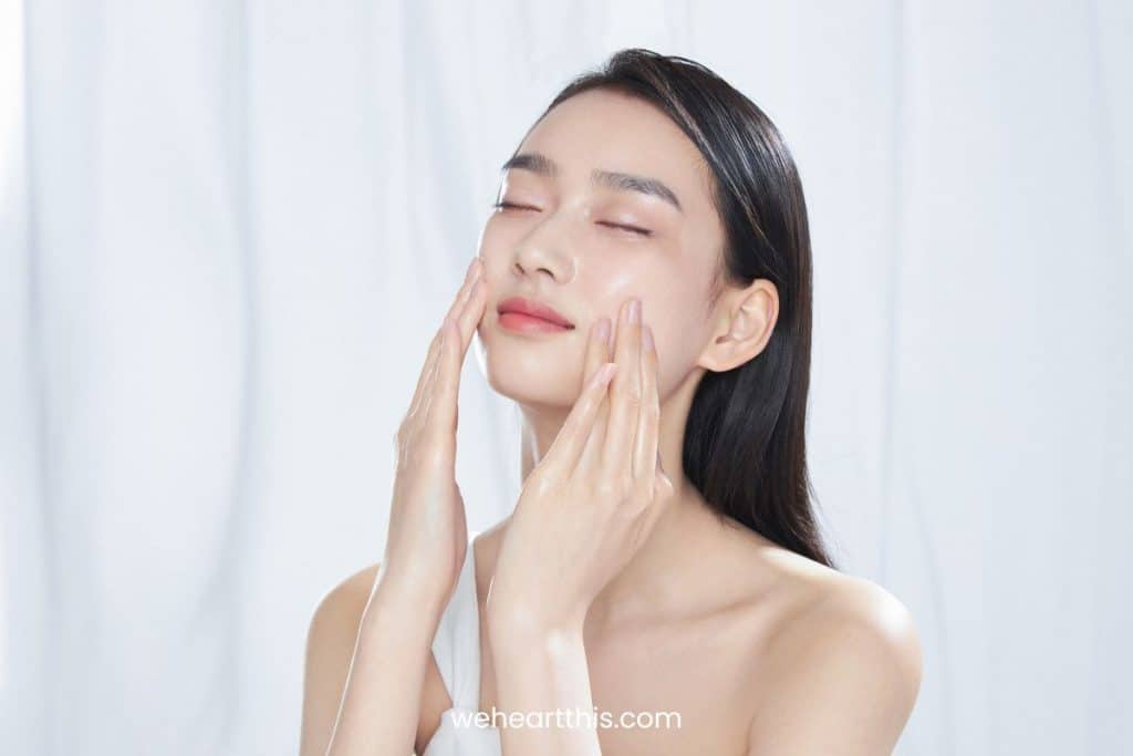an asian woman with long black hair is applying axis y dark spot correcting glow serum on her face