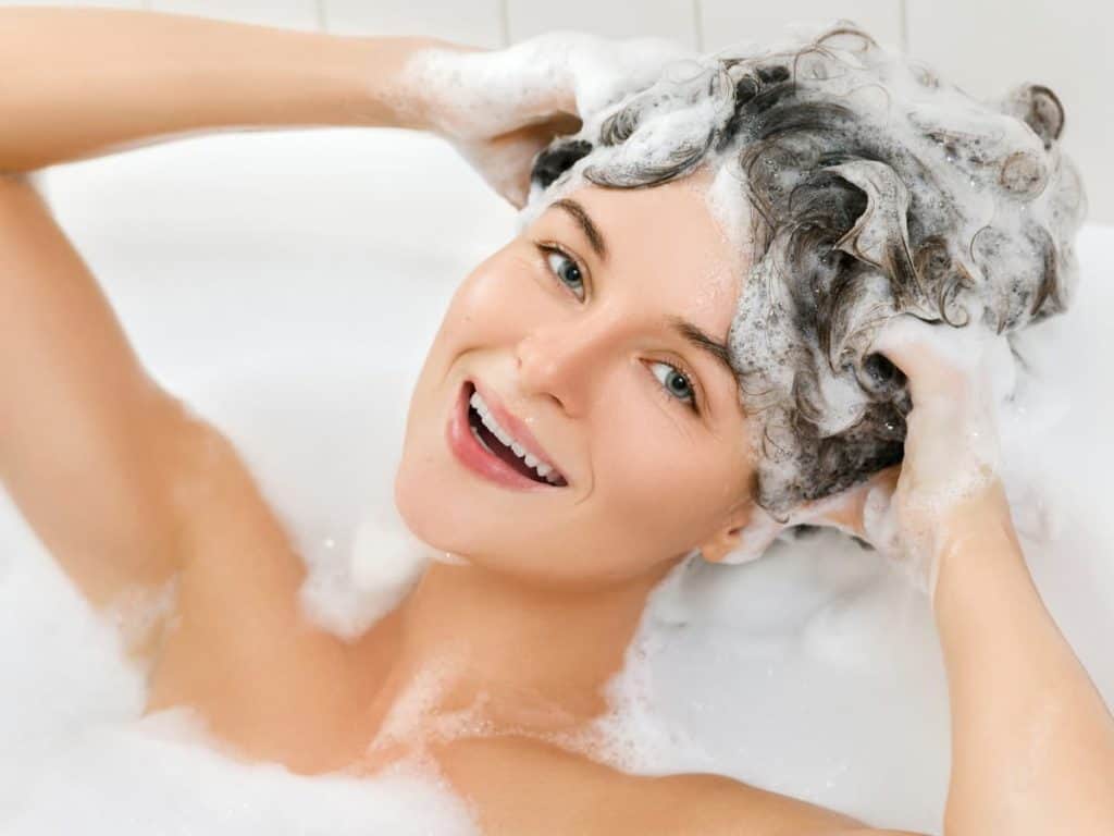 A  smiling woman is taking a bath with foam in her hair.