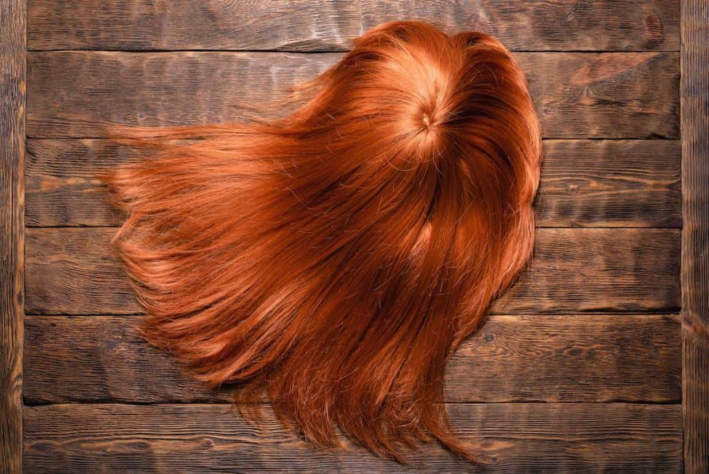 a synthetic hair with orange to red hair color is laid in a wooden table