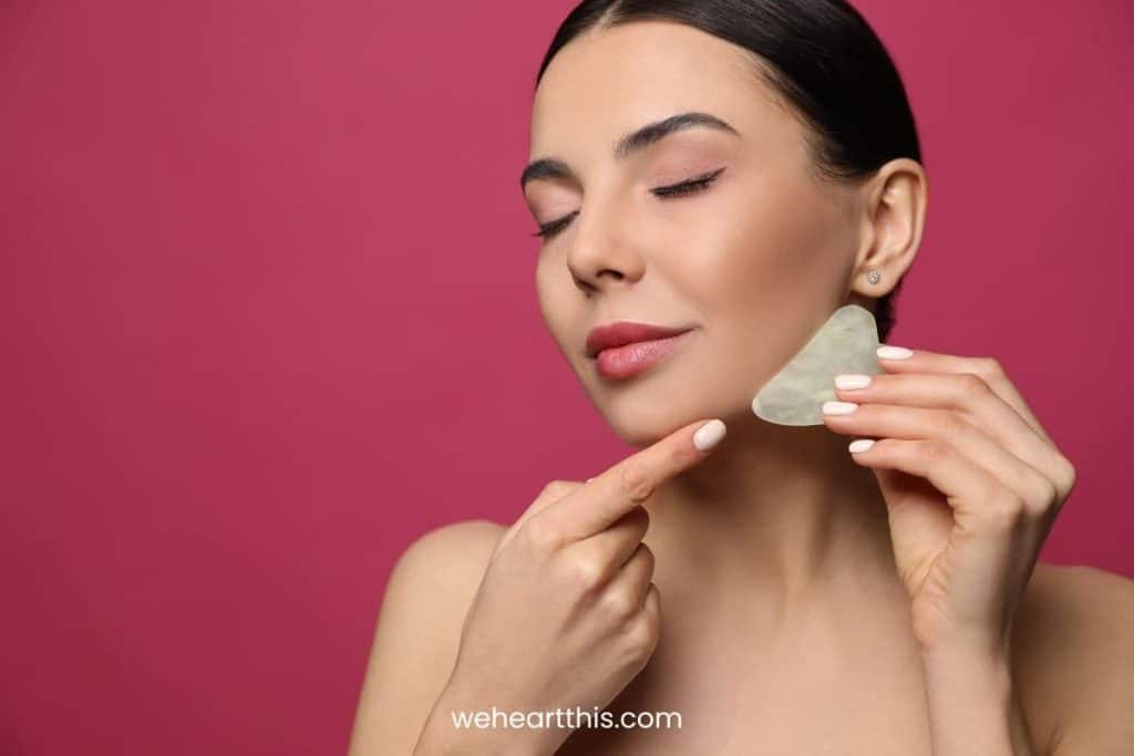 a girl using gua sha for face slimming in a dark pink background