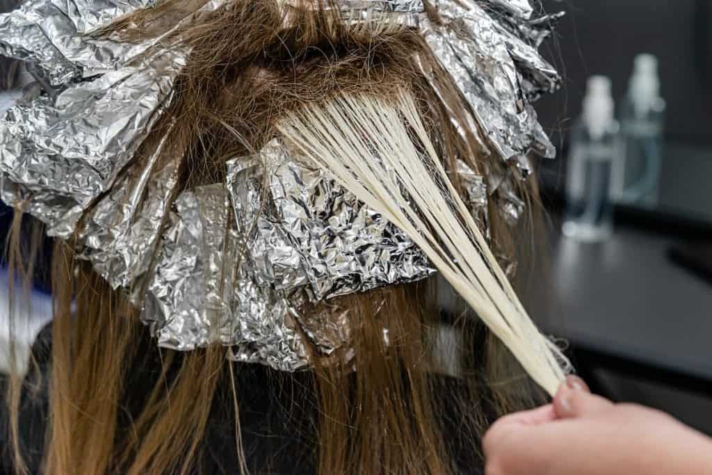 a hair stylist applying bleach on her client's hair and wrapping with aluminum foil after