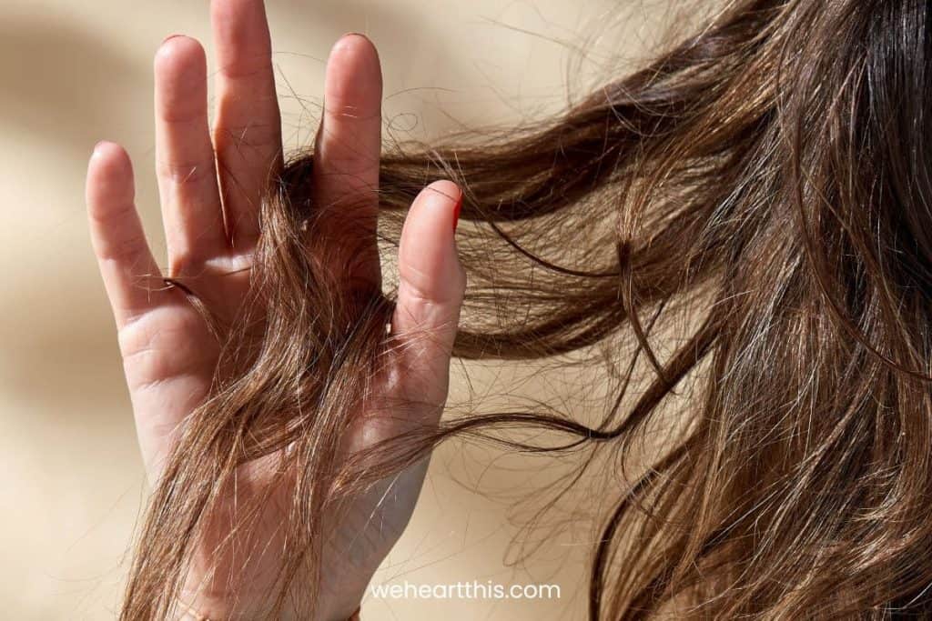 a close up image of a girl with wavy brown hair combing her hair using fingers