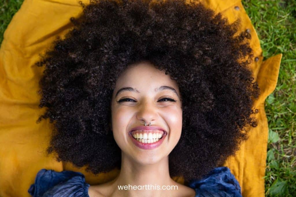 a young girl with high porosity hair is smiling widely at the camera while laying in a mustard cloth