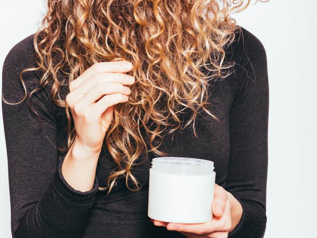 A cropped photo of a curly hair woman applying hair cream to her hair