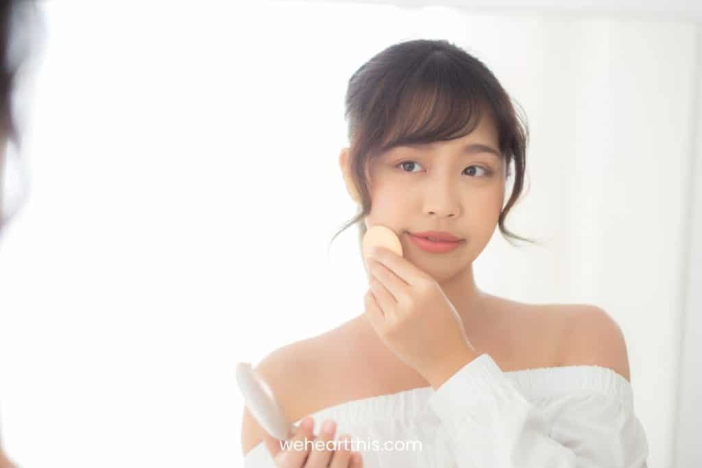 a young girl wearing white off shoulder top is applying missha magic cushion on her cheeks