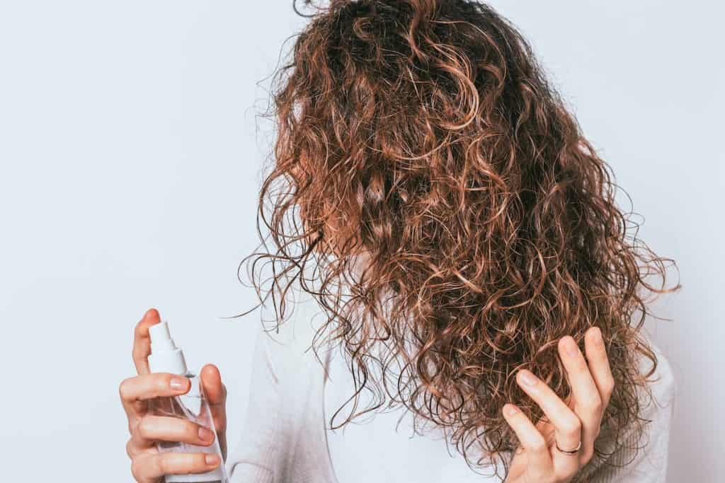 a woman with curly hair spraying rice water on her hair