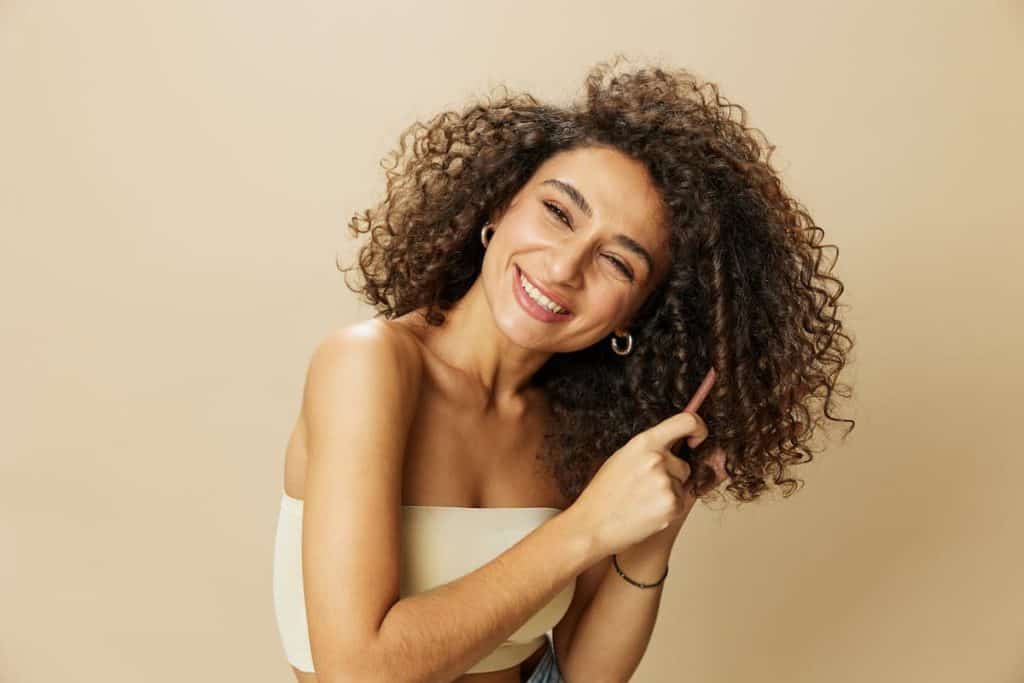 A woman smiling while combing her curly hair on a beige background