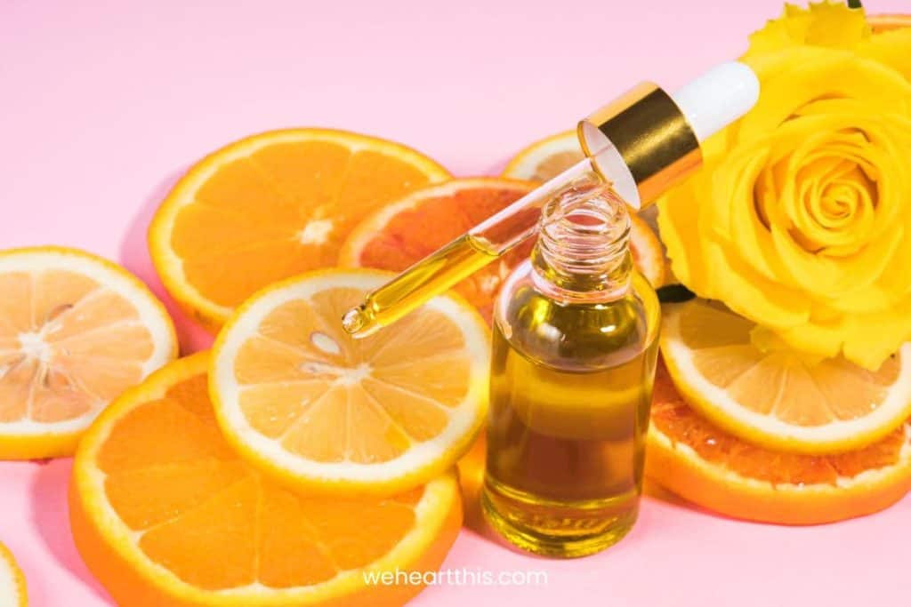 slices of orange are laid in a pink table with vitamin c serum and yellow flower