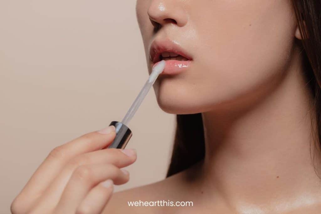 a close-up image of a woman applying lip gloss using a transparent applicator
