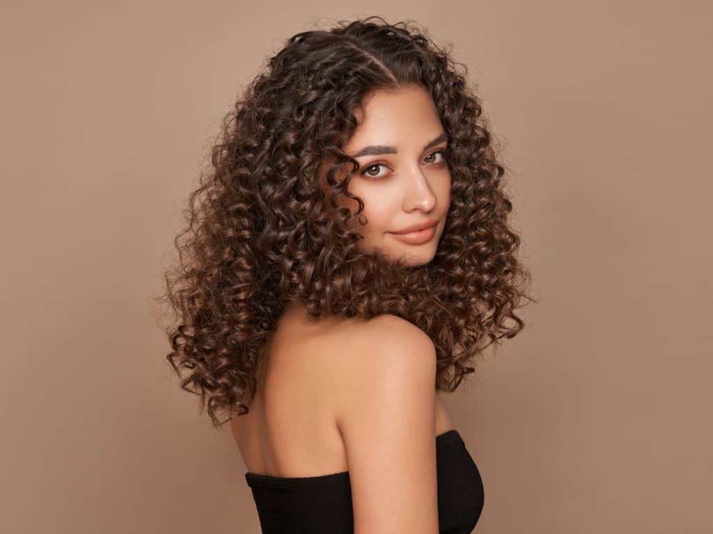 A young woman with curly hair posing on a brown background.