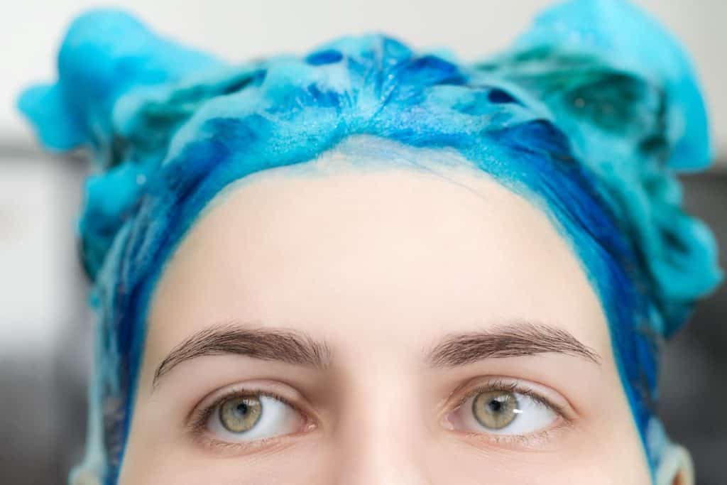 A woman is dyeing her hair blue with hair foam dye
