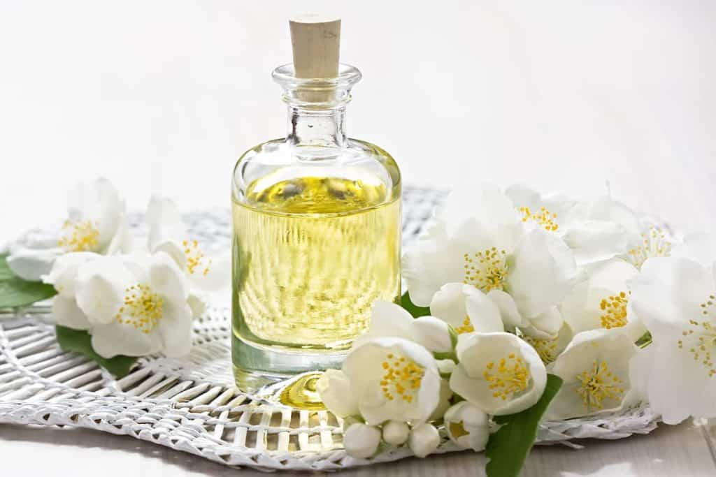 A bottle of jasmine essential oil on a table with white flowers.