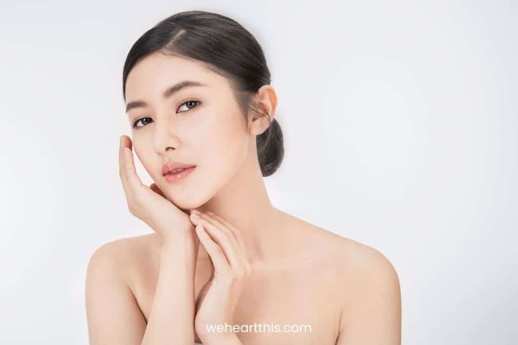 a young woman wearing tube top with her hair in a neat bun is posing at the camera highlighting her sculptured face after using gua sha