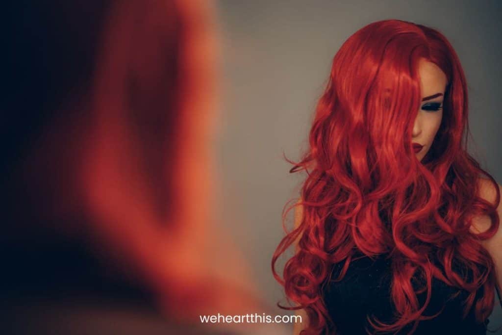 A red haired curly woman looking at herself in the mirror
