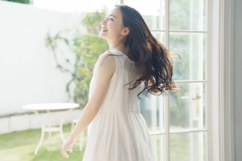 A young woman in a white dress standing in front of a window.