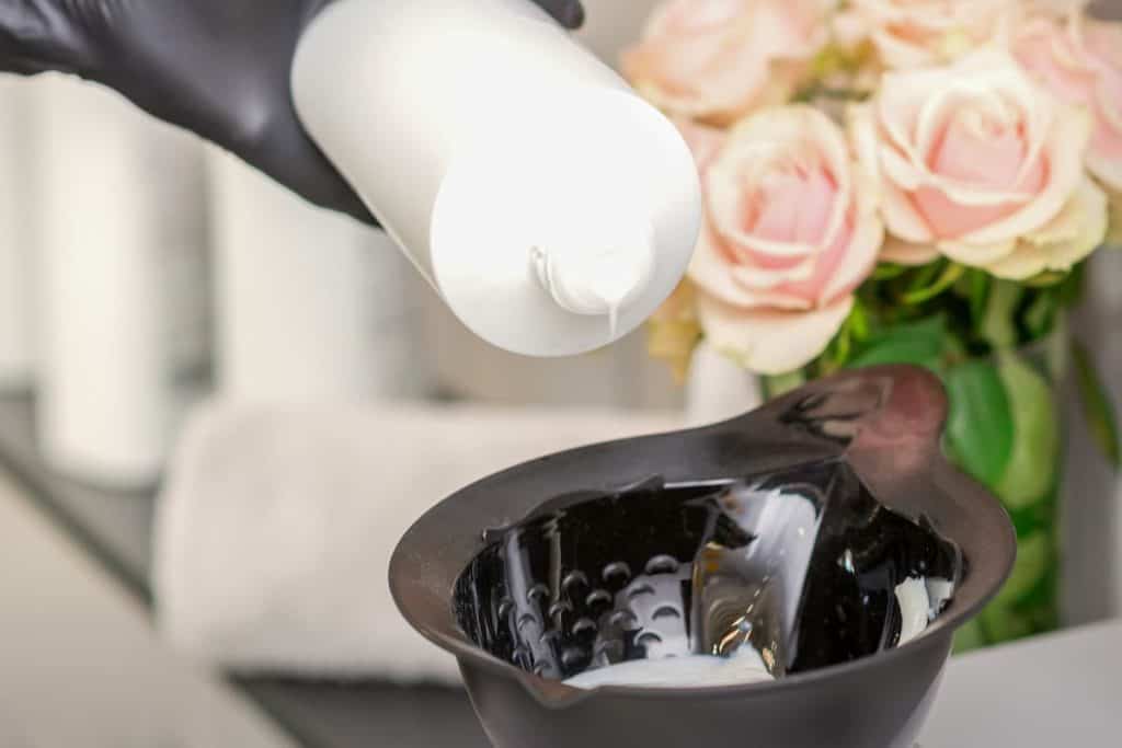 an individual is mixing hair dye in black mixing bowl while wearing black gloves