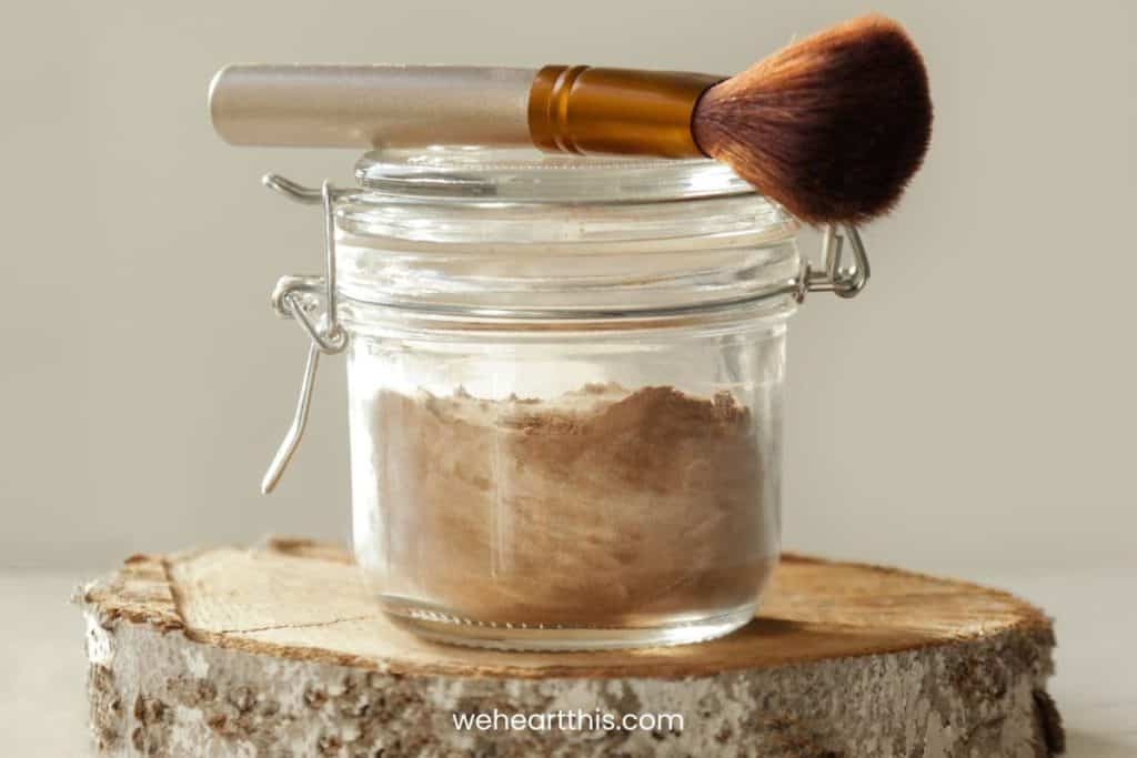 a mixture of powders inside a transparent glass jar for diy dry shampoo with a brush on top