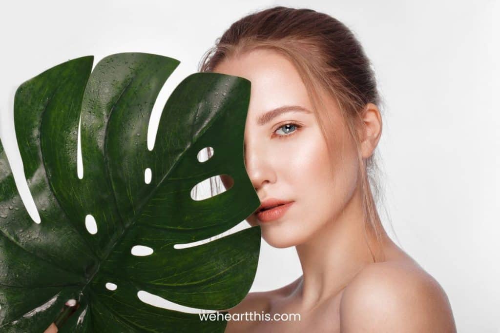 a woman with fresh make up holding a leaf covering the half of her face
