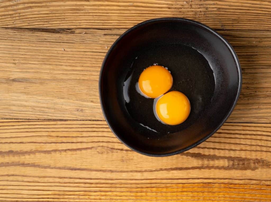 Two eggs in a black bowl on top of a wooden table