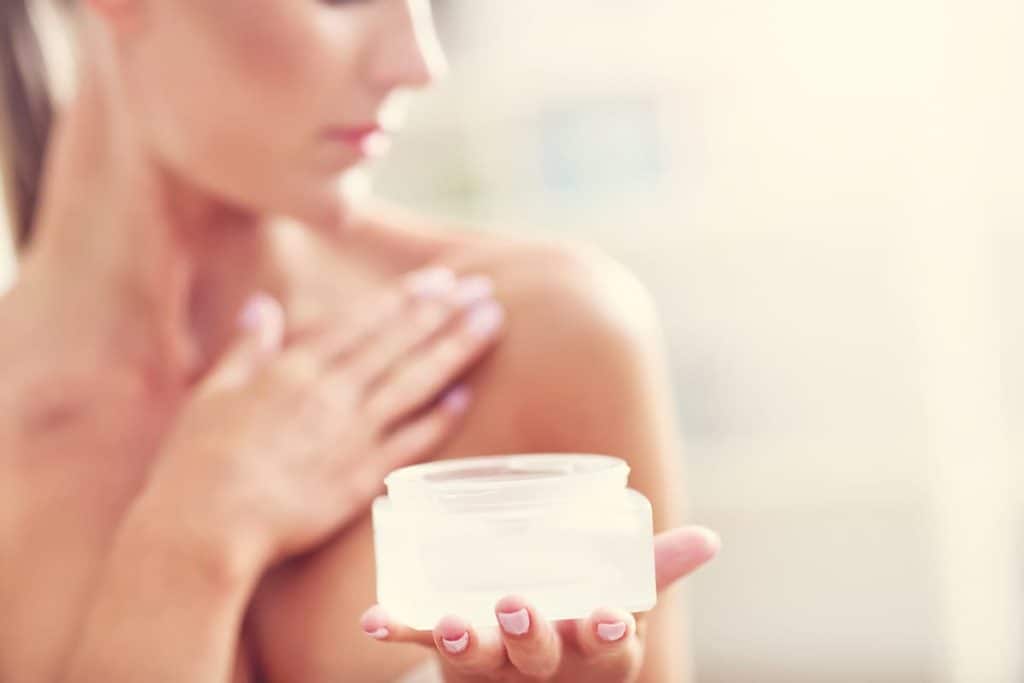 A cropped photo of a woman applying a balm on her shoulders while holding the product on her other hand