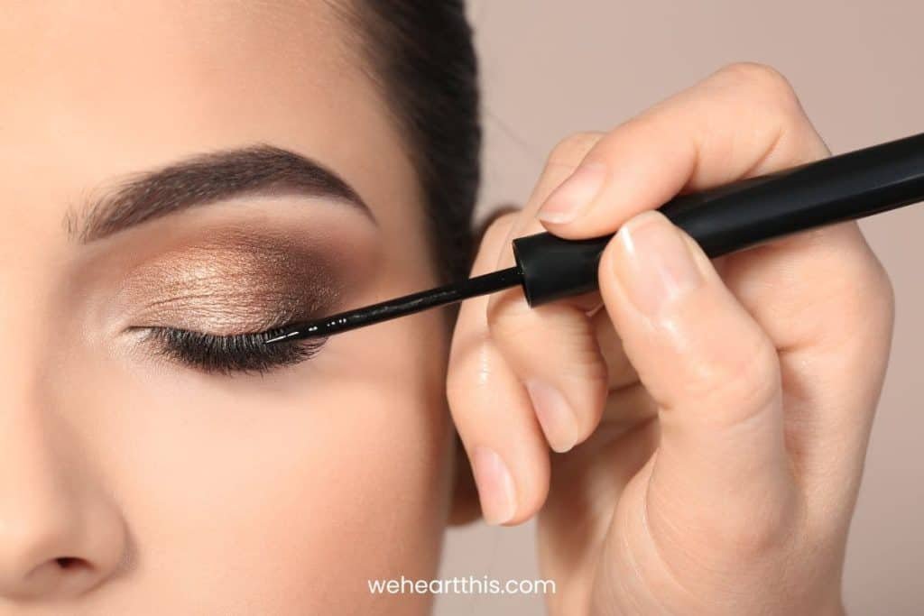 A woman closing her eyes while applying an eyeliner