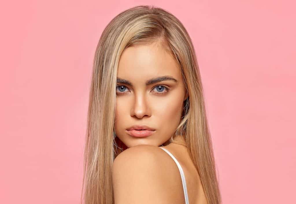 woman with long blonde hair and mineral makeup isolated on a pink background
