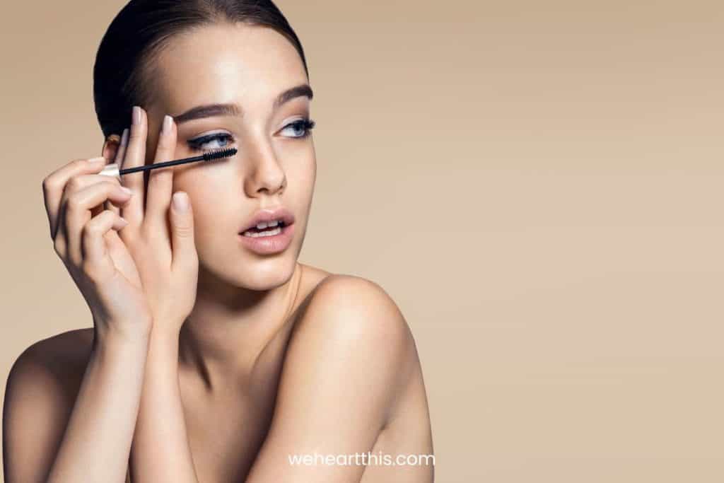 a young lady applying mascara on her eyelash extensions on a beige background