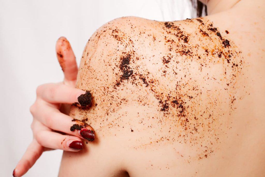 Back of a woman while exfoliating her skin using body scrub