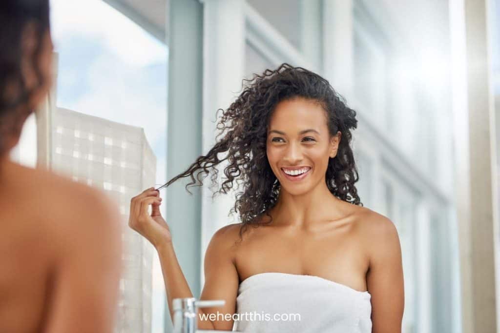 a beautiful black woman with body wrapped in a white towel is holding some of her hair strands after shower