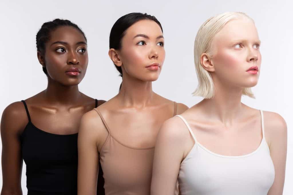 three beautiful woman with different skin color are wearing tank tops while looking sideways