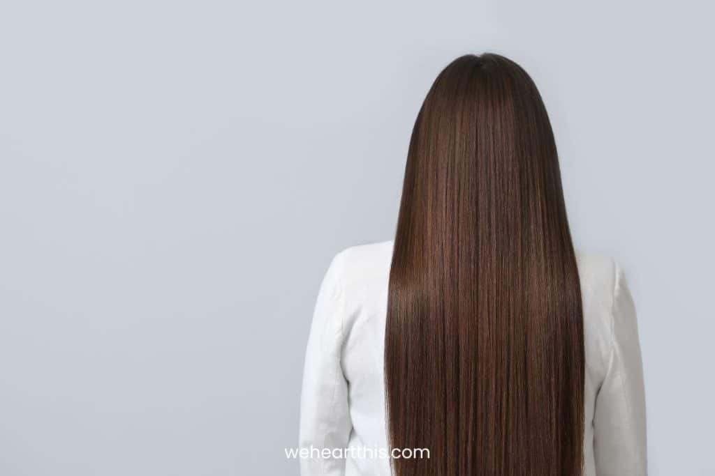 Back view of a woman with long, straight brown hair isolated on gray background
