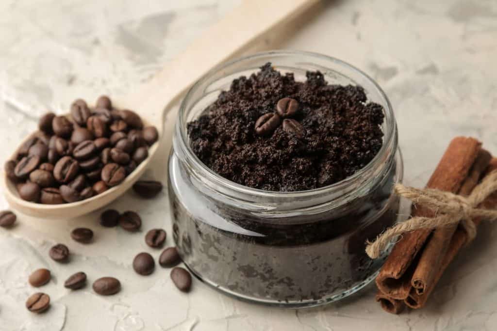 A jar of homemade coffee scrub and a spoon of coffee beans on a beige surface